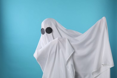 Photo of Creepy ghost. Person covered with white sheet on light blue background, space for text