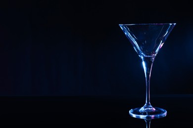 Photo of Empty clean martini glass on mirror table against black background, space for text