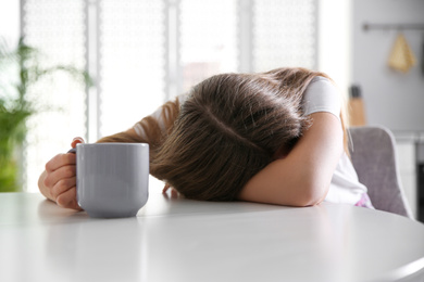 Young woman with cup of drink sleeping at home in morning