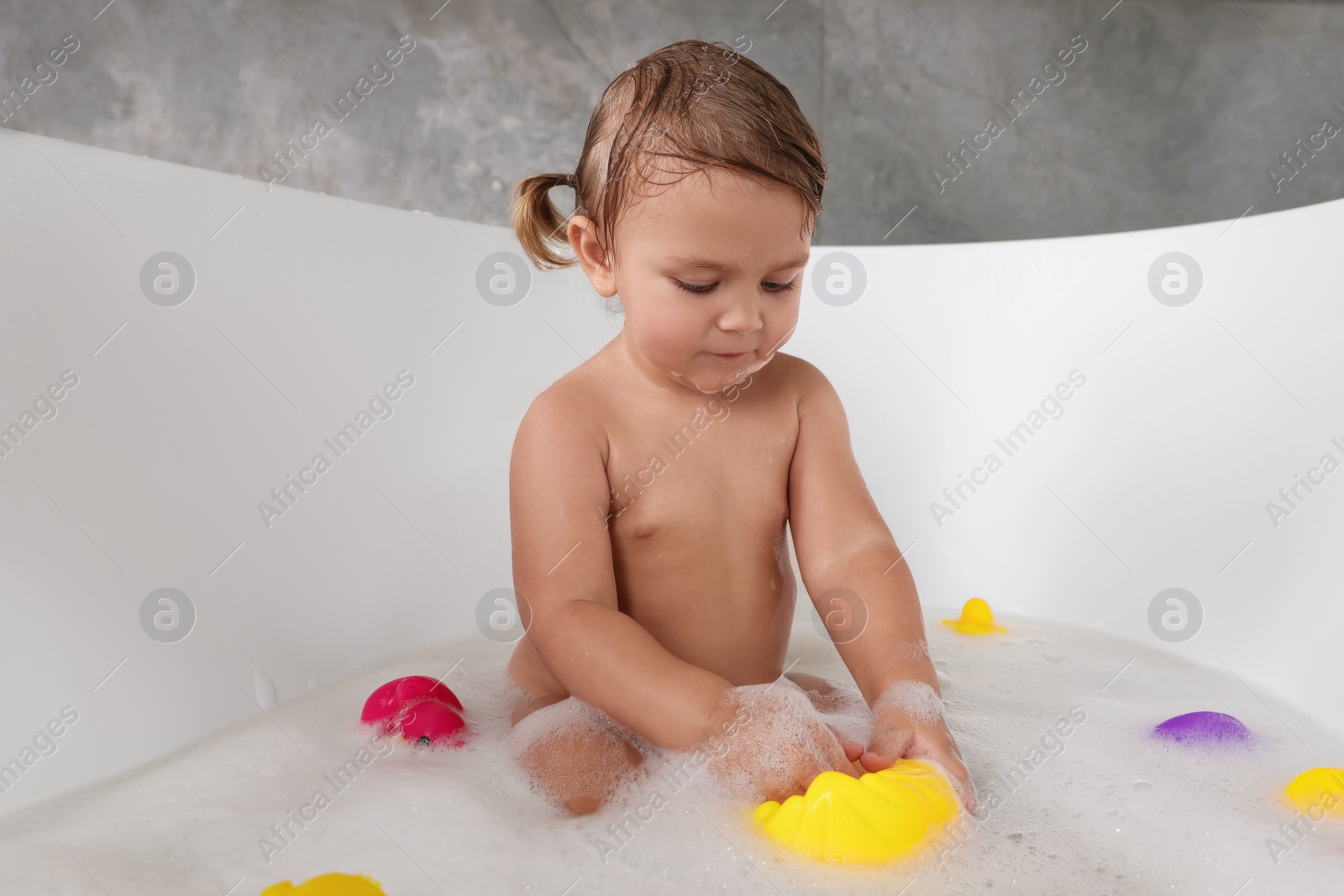 Photo of Cute little girl taking bubble bath with toys indoors