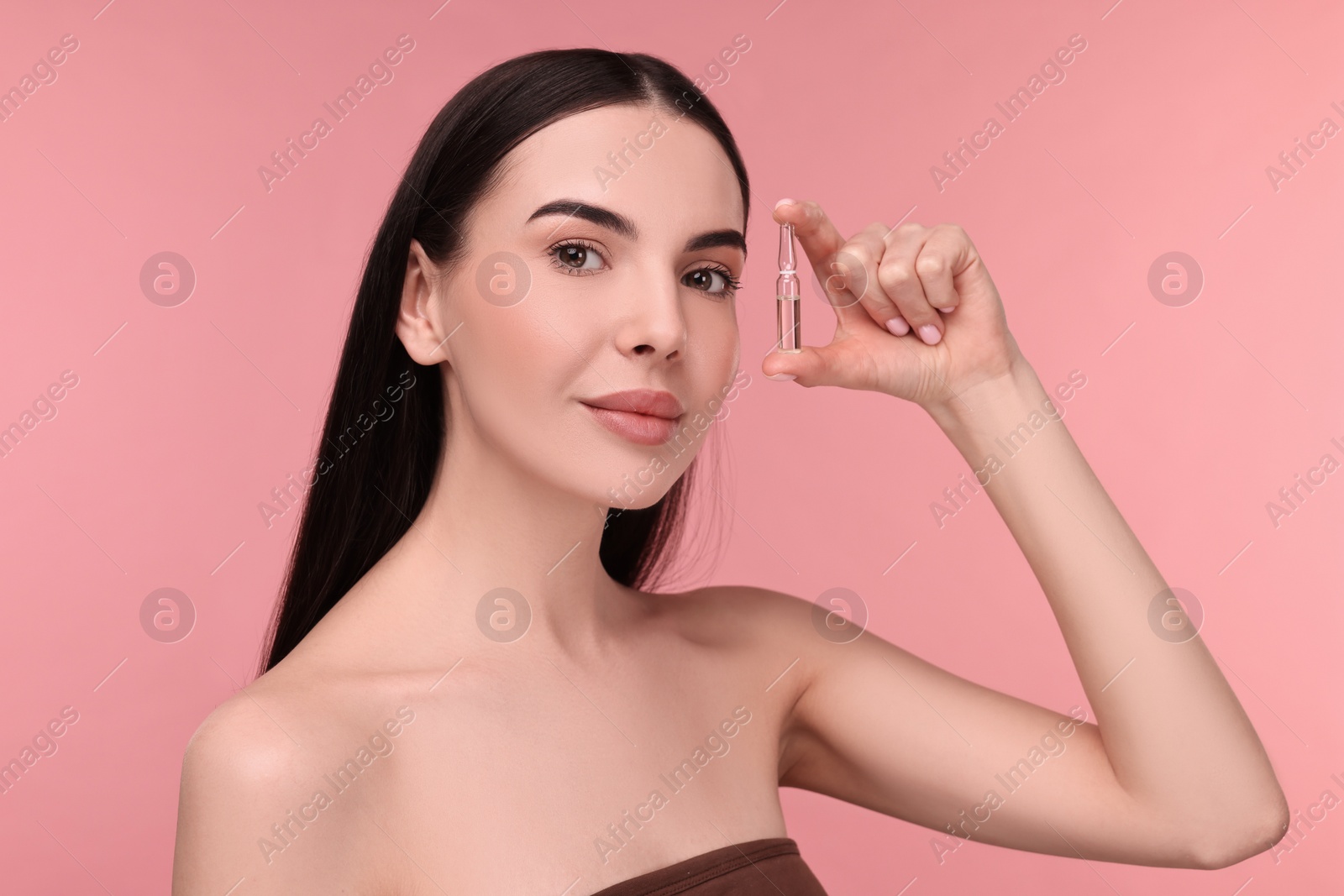 Photo of Beautiful young woman holding skincare ampoule on pink background