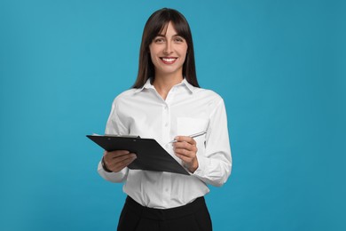 Photo of Happy secretary with clipboard and pen on light blue background