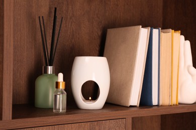 Photo of Aroma lamp, bottle of oil, books and reed diffuser on wooden shelf indoors