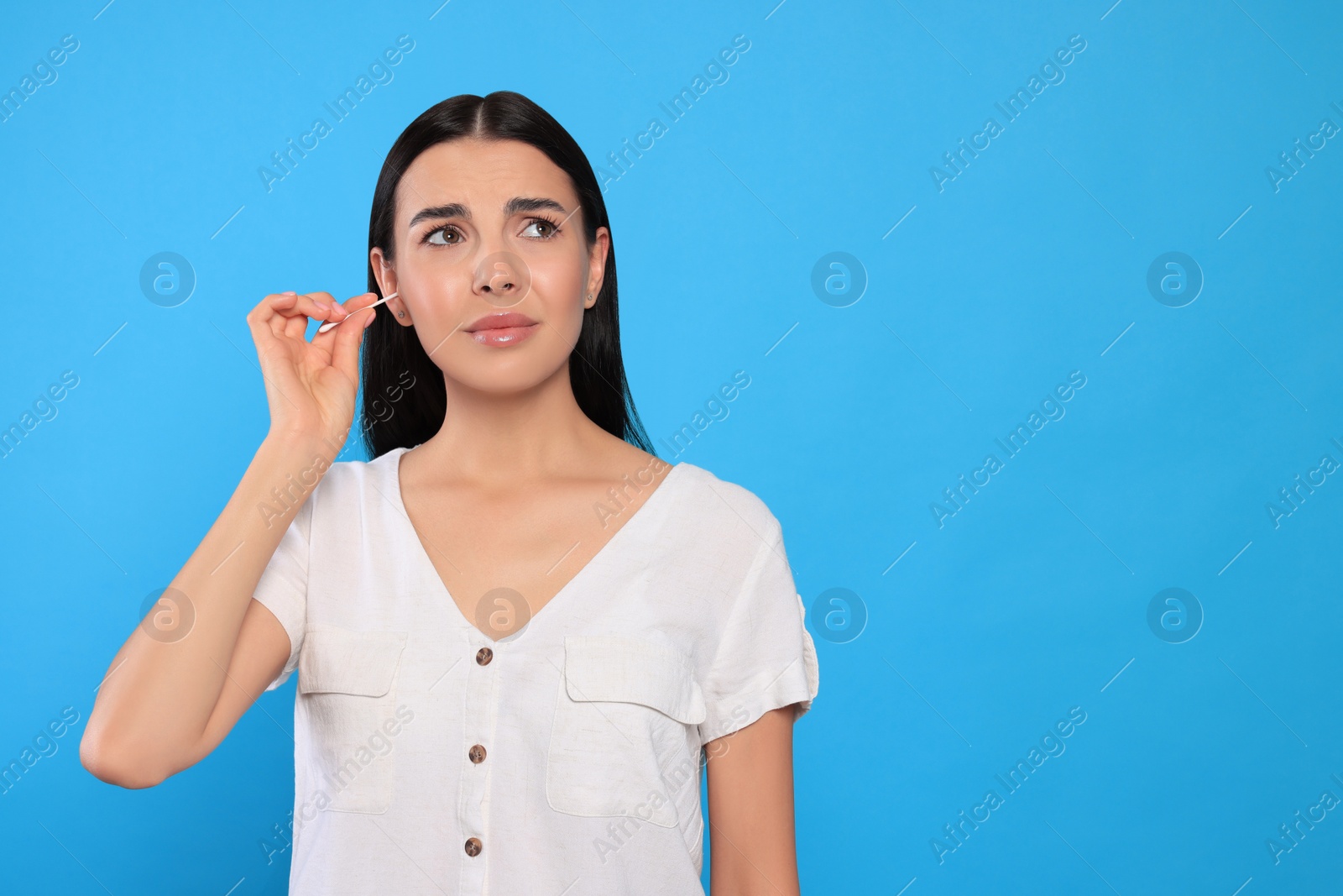 Photo of Young woman cleaning ear with cotton swab on light blue background. Space for text