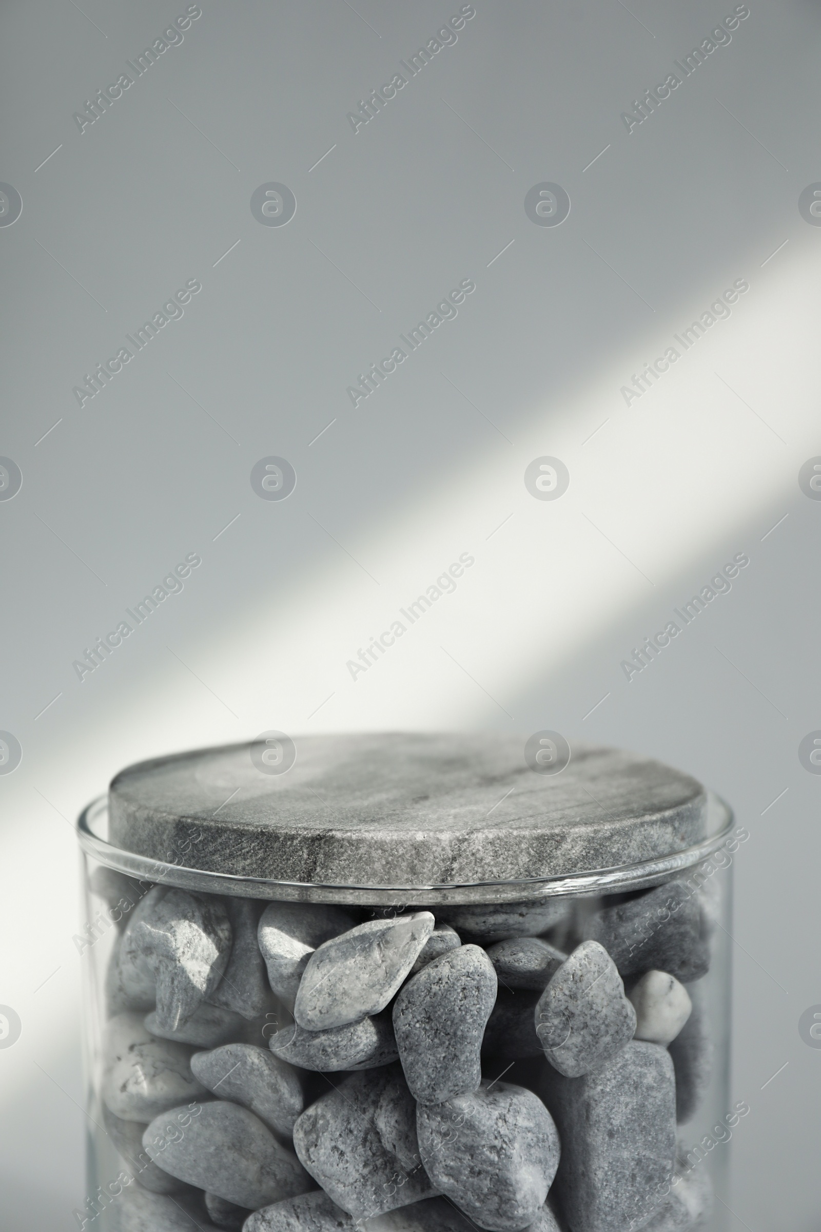 Photo of Presentation for product. Glass container with stones on light grey background. Space for text