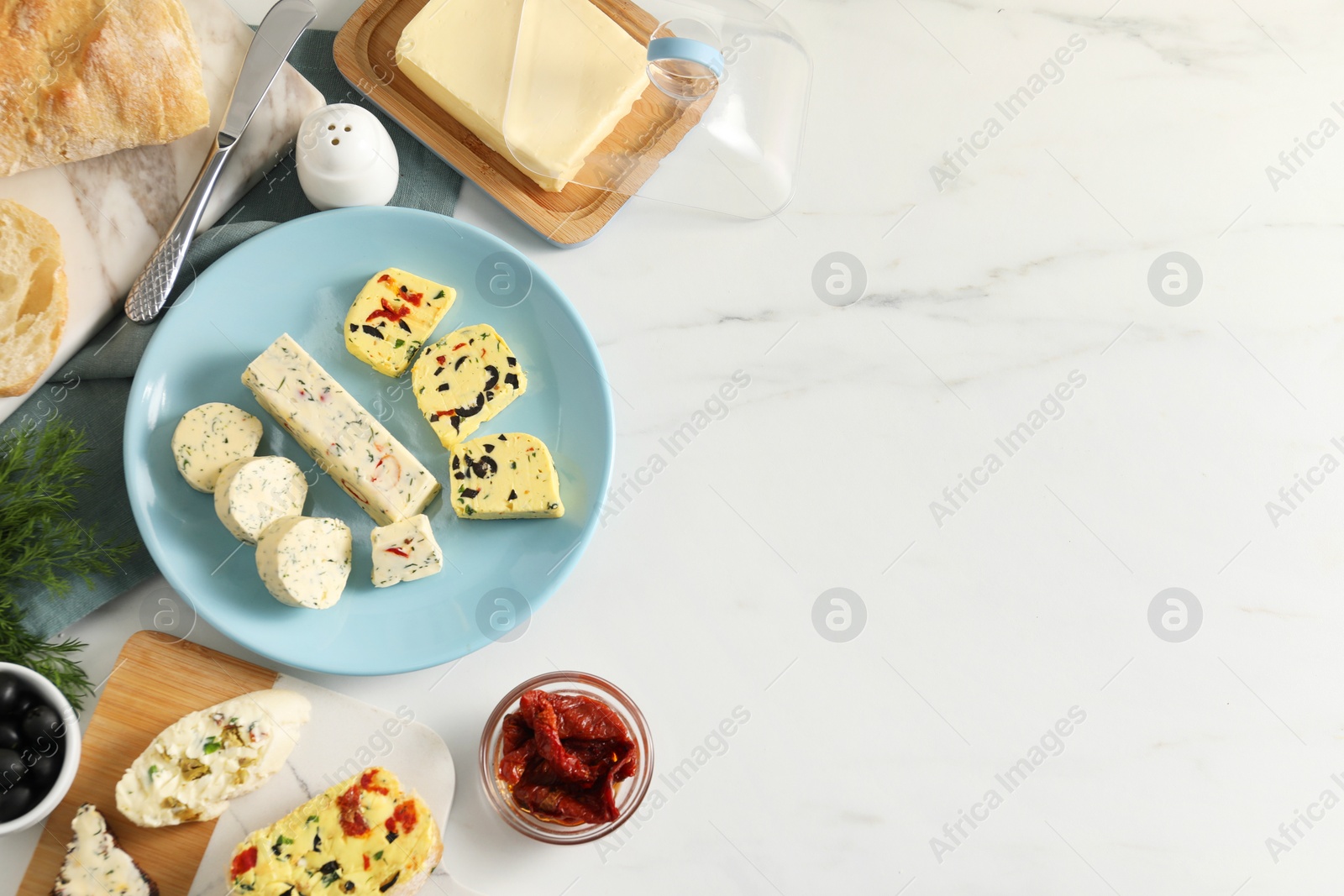 Photo of Different types of tasty butter, dill, chili and bread on white marble table, top view. Space for text