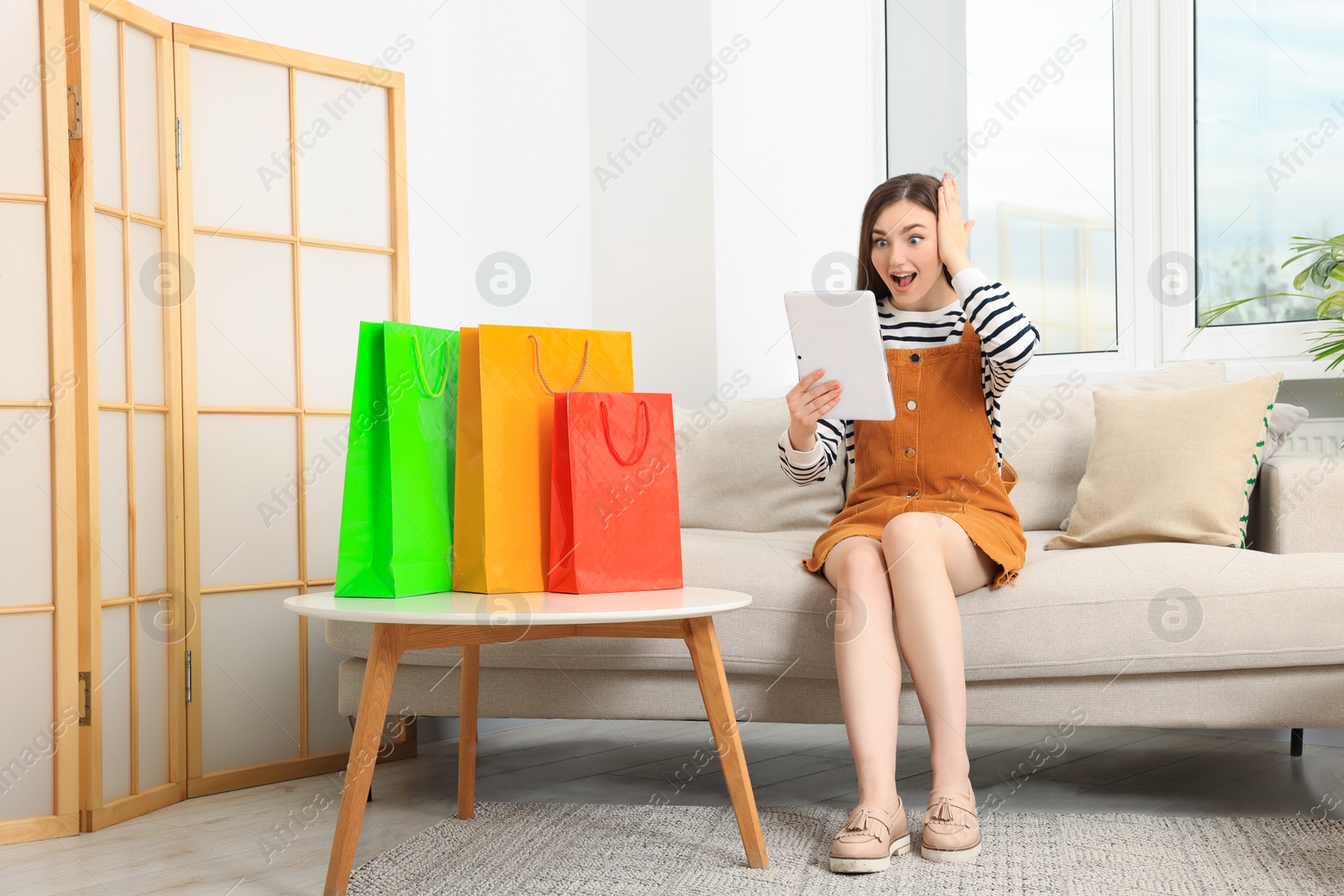 Photo of Special Promotion. Emotional woman looking at tablet on sofa indoors