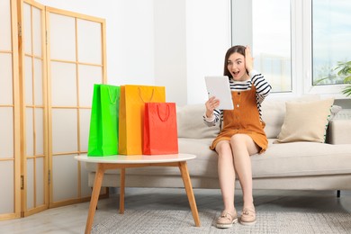 Photo of Special Promotion. Emotional woman looking at tablet on sofa indoors