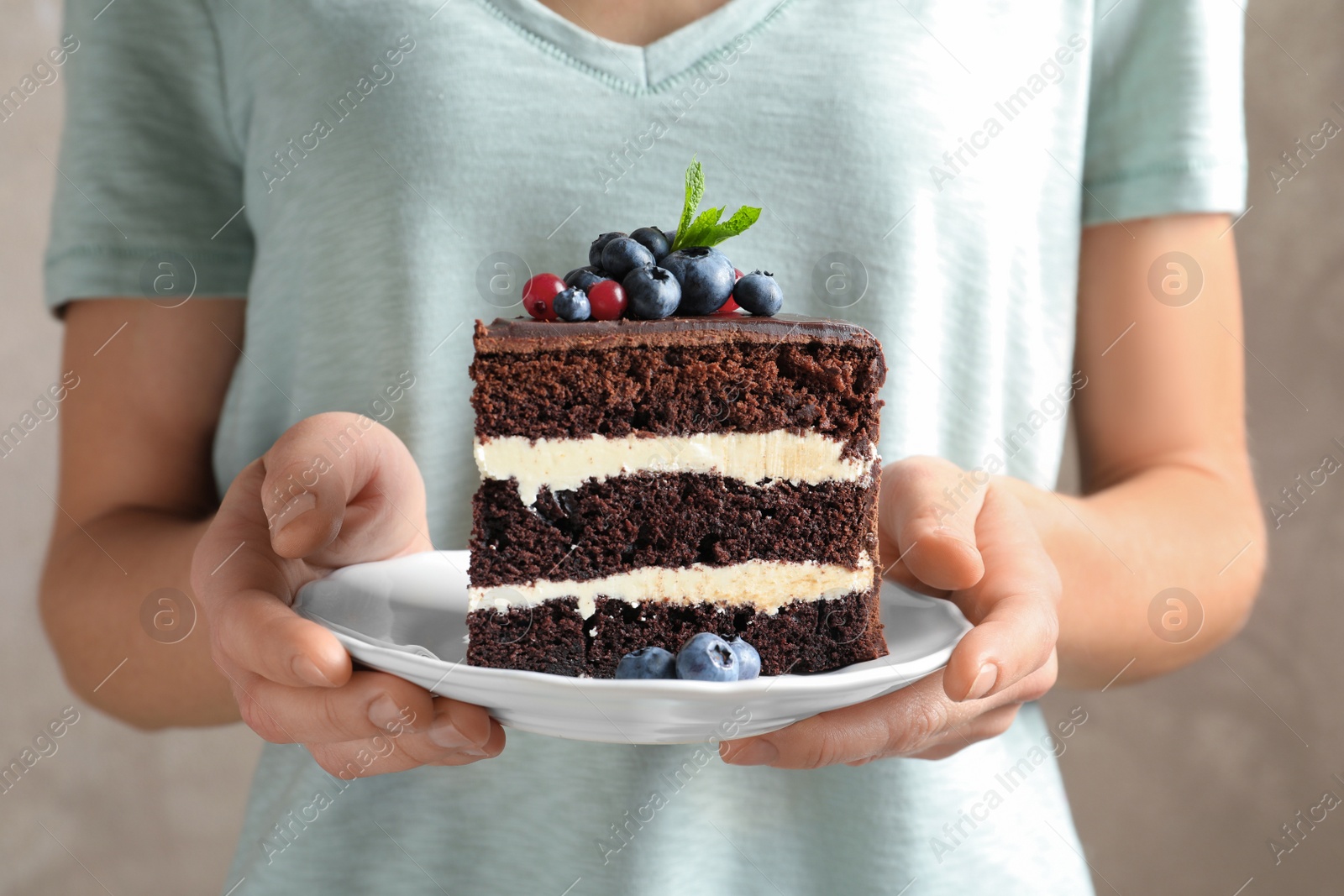 Photo of Woman holding plate with slice of chocolate sponge berry cake, closeup