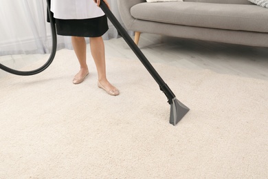 Photo of Chambermaid removing dirt from carpet with vacuum cleaner indoors, closeup. Space for text