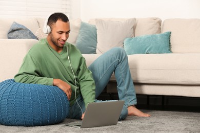 Photo of Smiling African American man in headphones with laptop near sofa at home