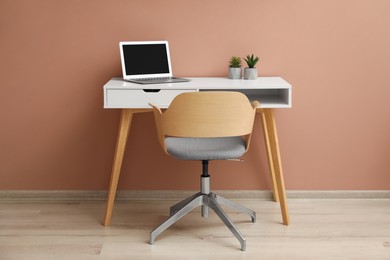 Photo of Stylish workplace with laptop and comfortable chair near beige wall indoors. Interior design