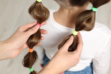 Photo of Professional stylist braiding girl's hair indoors, closeup