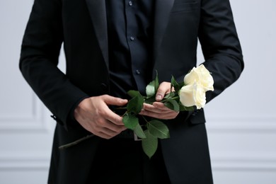 Photo of Man with rose flowers near white wall, closeup. Funeral ceremony
