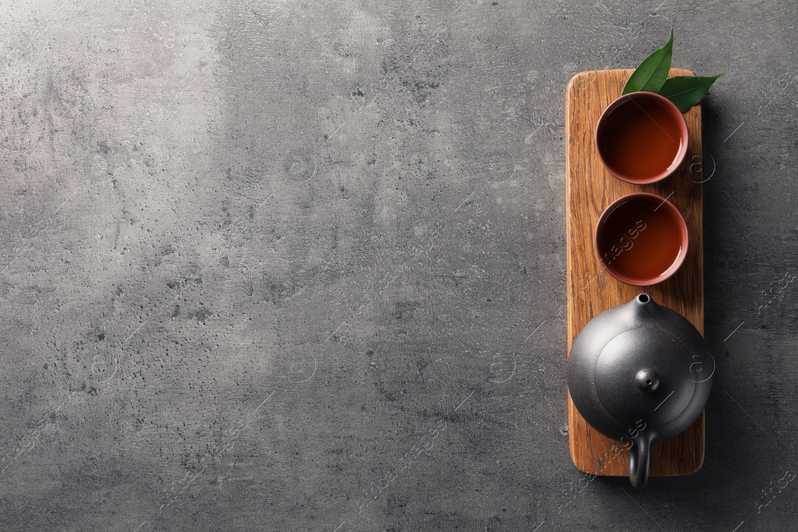 Photo of Board with cups and teapot of freshly brewed oolong on grey background, top view with space for text