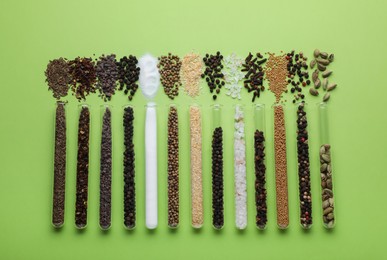 Photo of Test tubes with various spices on green background, flat lay