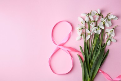 Photo of Beautiful snowdrops and number 8 made of ribbon on pink background, flat lay. Space for text