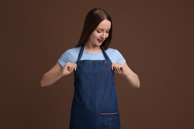 Beautiful young woman wearing kitchen apron on brown background. Mockup for design