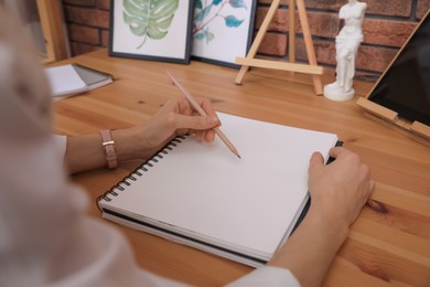 Photo of Woman drawing in sketchbook with pencil at wooden table indoors, closeup