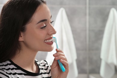 Young woman brushing her teeth with plastic toothbrush in bathroom