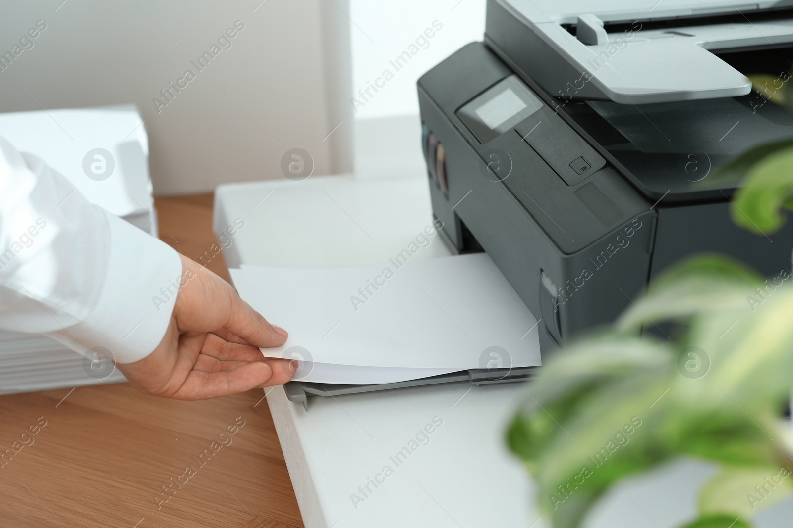 Photo of Woman loading paper into printer at wooden table indoors, closeup