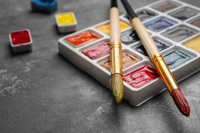 Photo of Plastic palette with colorful paints and brushes on grey table