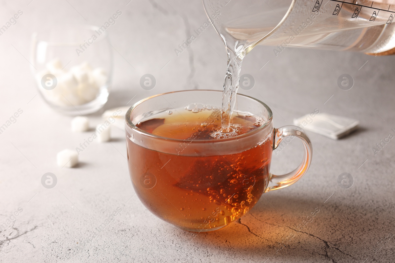 Photo of Pouring hot water into cup with tea bag on light grey textured table, closeup