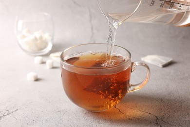 Photo of Pouring hot water into cup with tea bag on light grey textured table, closeup