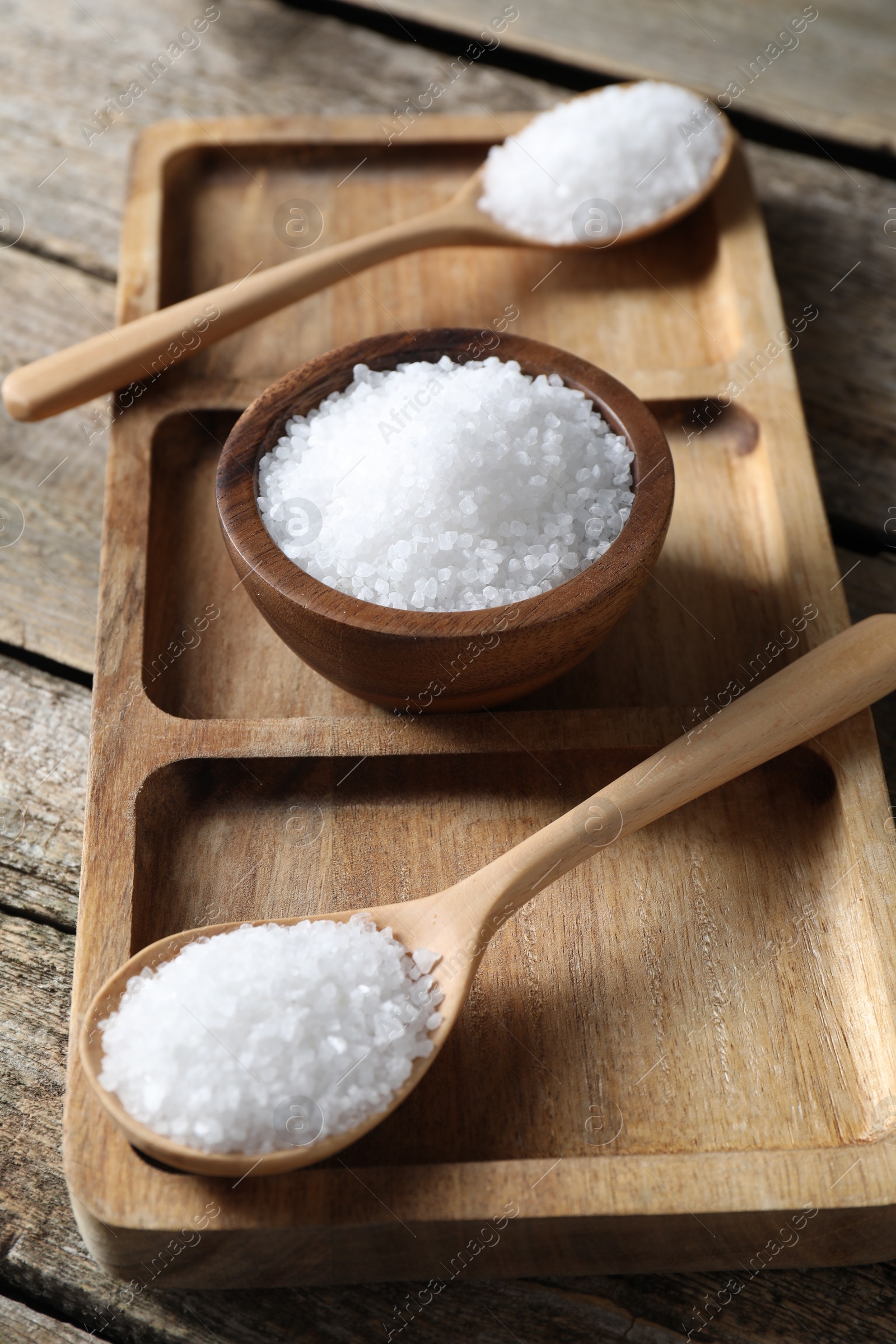 Photo of Organic salt in bowl and spoons on wooden table, closeup