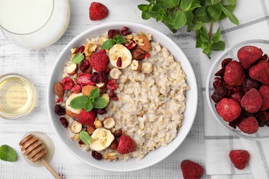 Photo of Delicious oatmeal with freeze dried berries, banana, nuts and mint served on white wooden table, flat lay