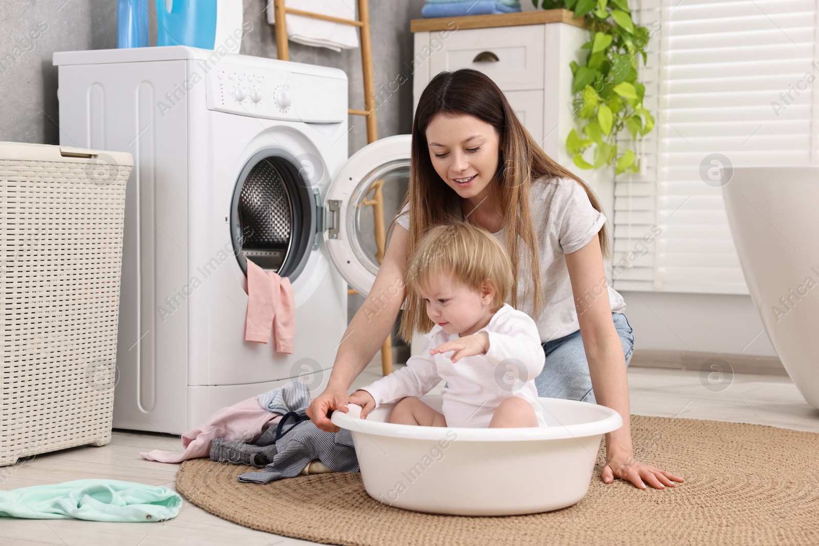 Photo of Happy mother with her daughter having fun while washing baby clothes in bathroom