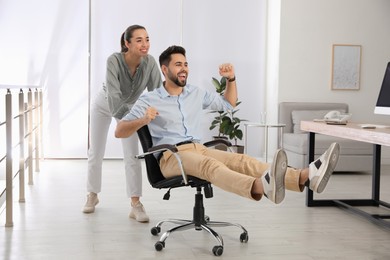 Photo of Office employee giving her colleague ride in chair at workplace