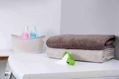 Towels and measuring scoop with powder on washing machine indoors, space for text. Laundry day