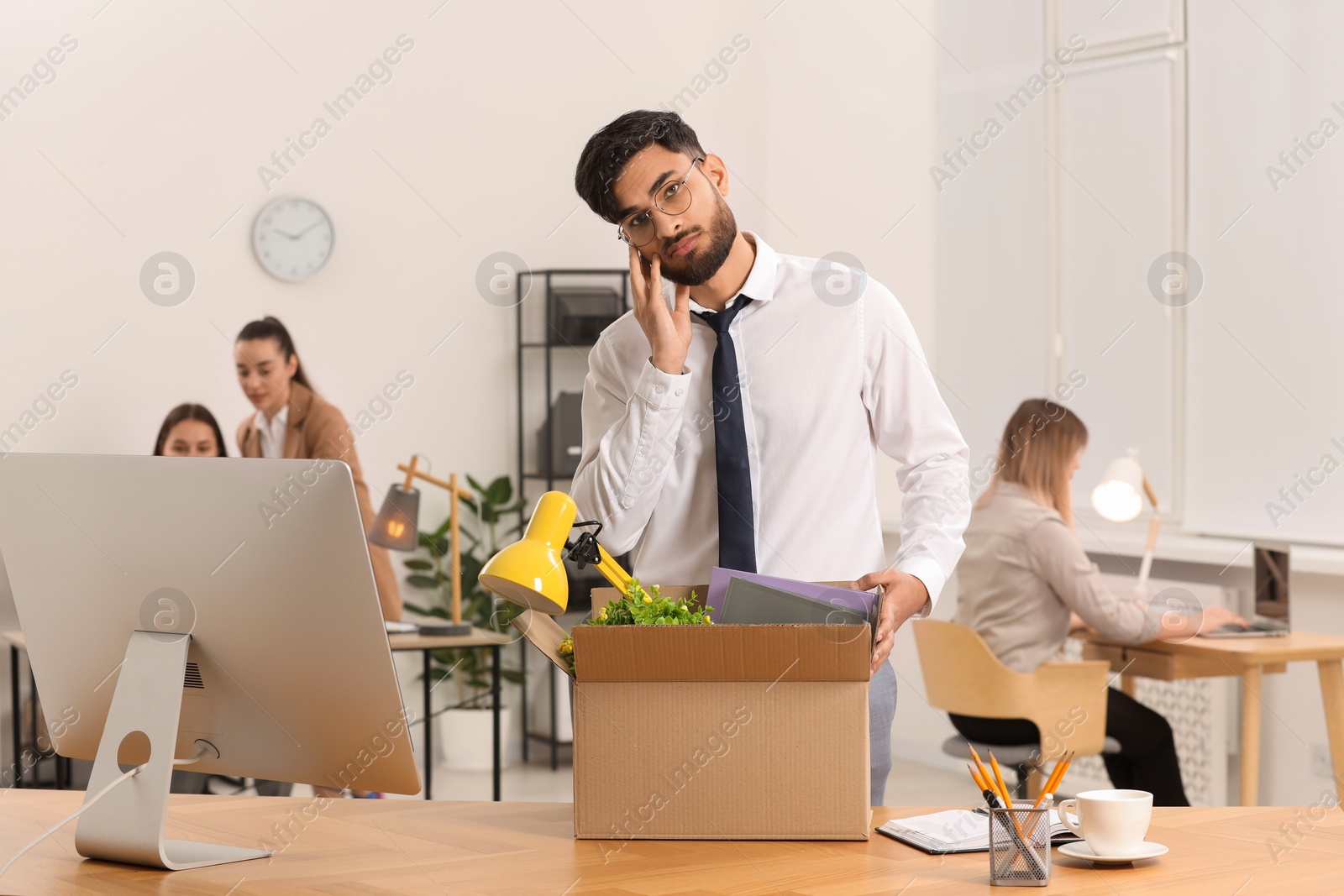 Photo of Unemployment problem. Frustrated man with box of personal belongings at table in office