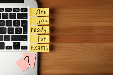 Photo of Laptop with question Are You Ready For Exams? made of post note stickers on wooden table, flat lay. Space for text