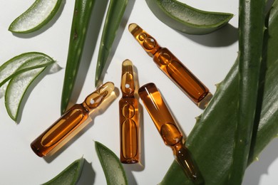 Photo of Skincare ampoules and aloe leaves on white background, flat lay