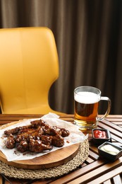 Tasty chicken wings, sauces and mug of beer on wooden table, space for text. Delicious snack