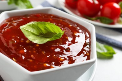 Photo of Spicy chili sauce with basil on light table, closeup