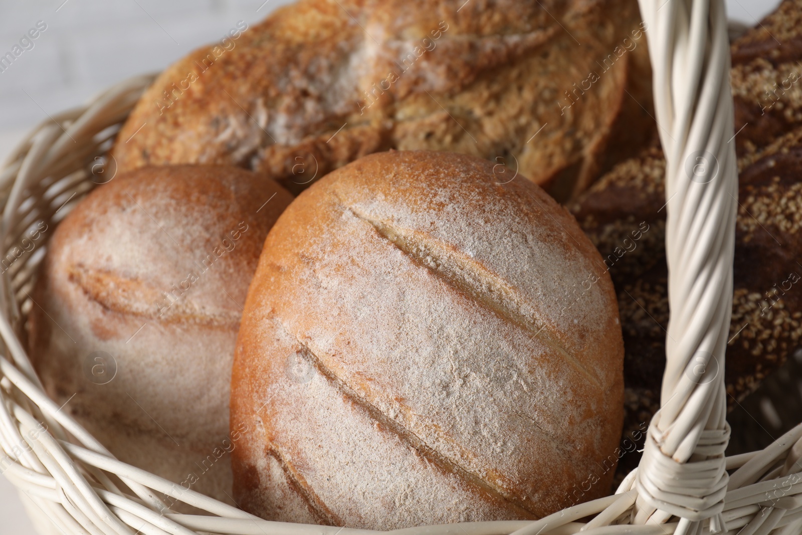 Photo of Different types of bread in wicker basket, closeup