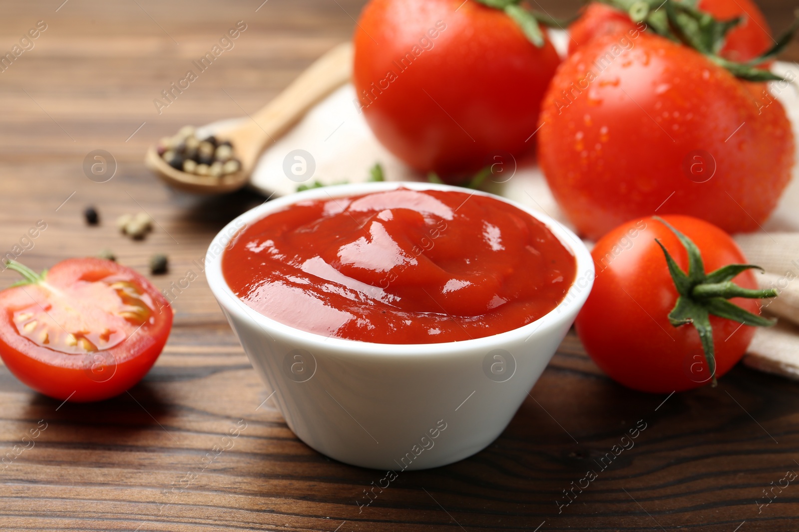 Photo of Delicious ketchup in bowl and tomatoes on wooden table, closeup