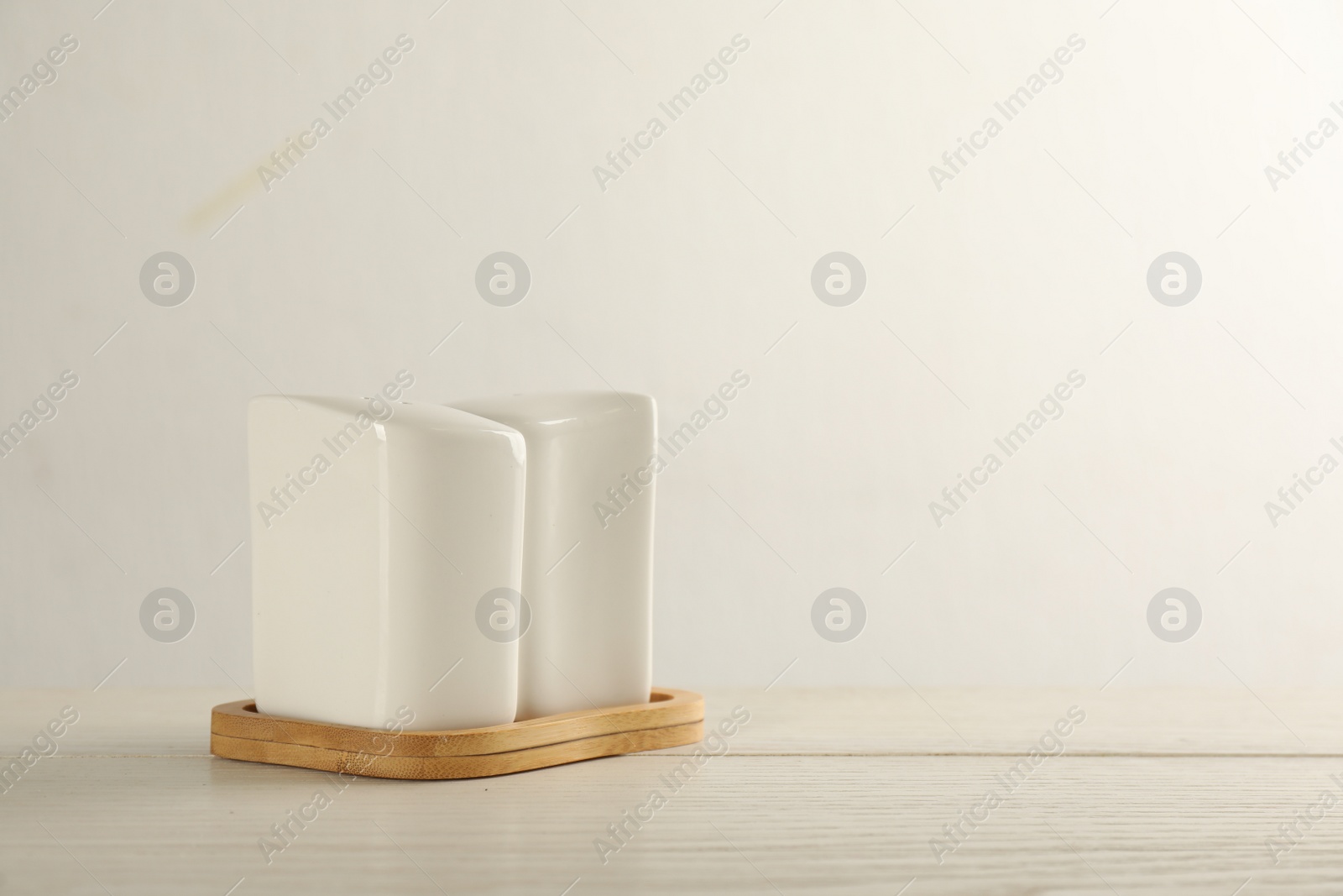 Photo of Ceramic salt and pepper shakers with stand on wooden table against white background. Space for text