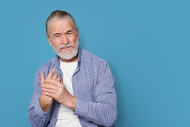 Photo of Senior man suffering from pain in hand on light blue. Arthritis symptoms
