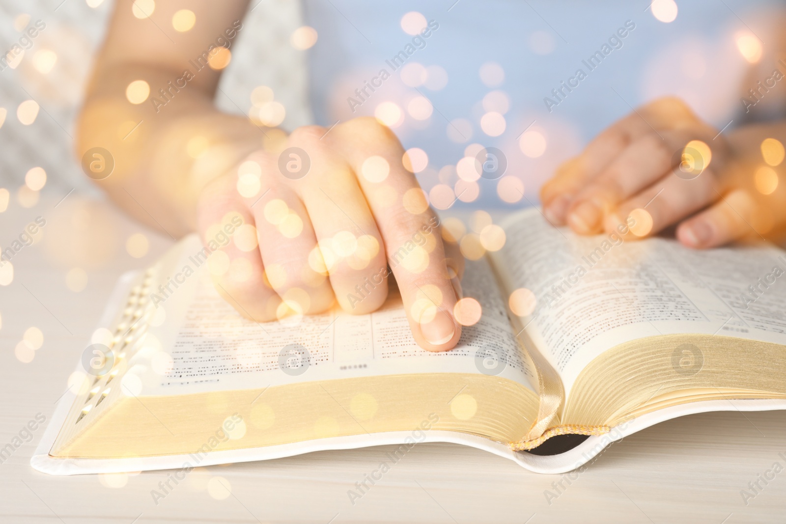 Image of Woman reading Bible at white wooden table, closeup. Bokeh effect