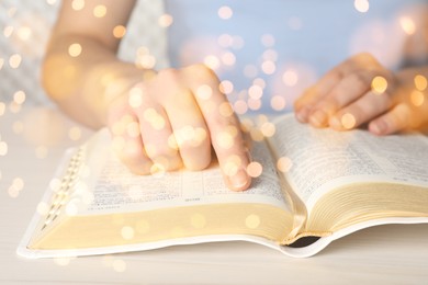 Image of Woman reading Bible at white wooden table, closeup. Bokeh effect