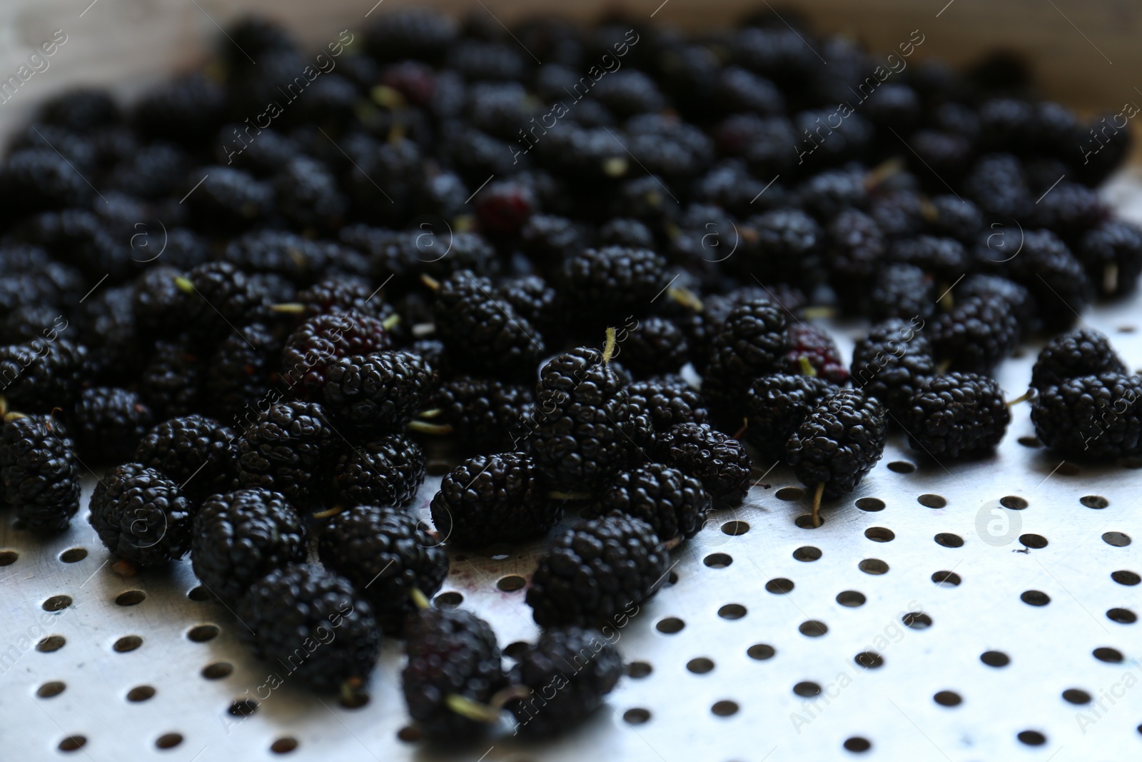 Photo of Heap of delicious ripe black mulberries in colander, closeup