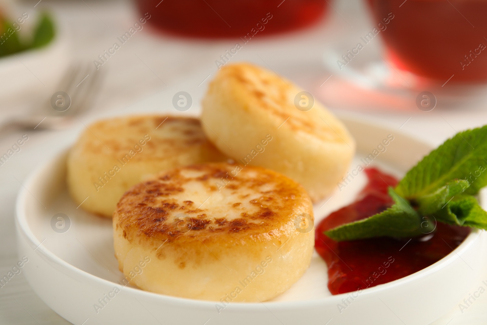 Photo of Delicious cottage cheese pancakes with jam and mint on table, closeup