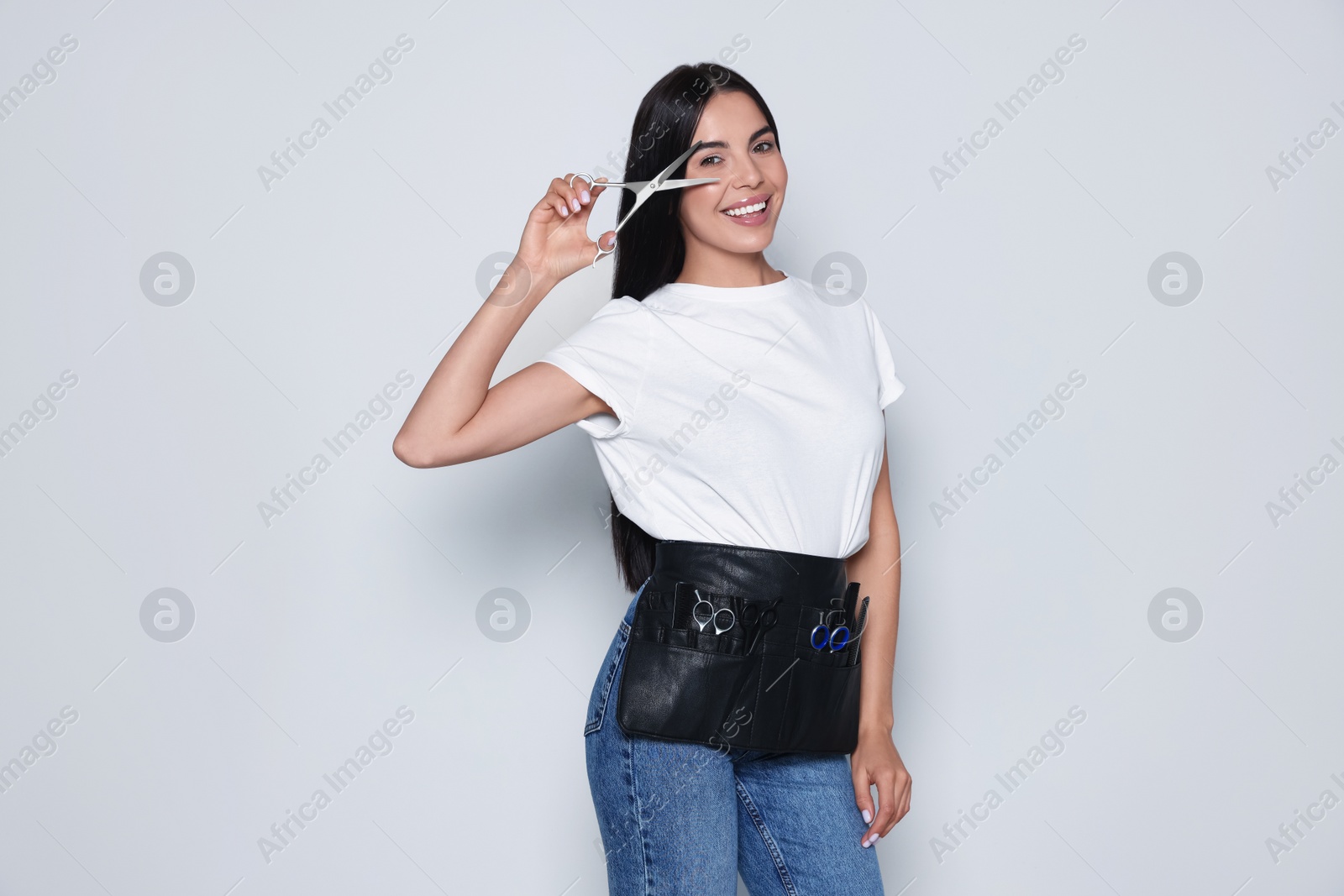 Photo of Portrait of happy hairdresser with professional scissors on light background