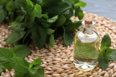 Photo of Bottle of essential oil and mint on wicker mat, closeup