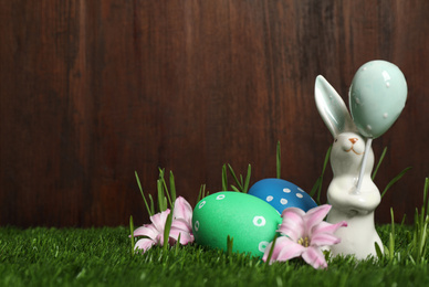 Photo of Colorful Easter eggs, rabbit and flowers on green grass. Space for text