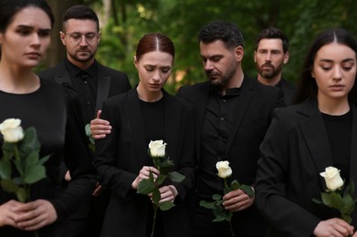Photo of Funeral ceremony. Sad people with white rose flowers mourning outdoors